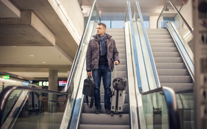 Man staat met een bagage op een roltrap op een vliegveld