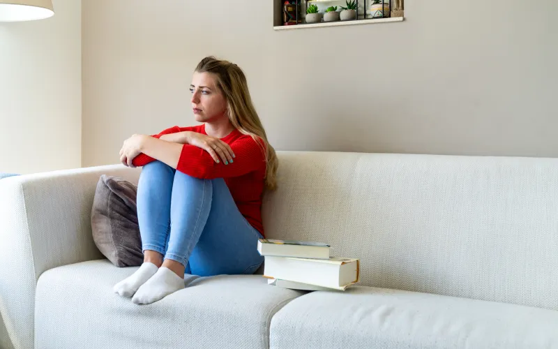 Jonge vrouw zit op de bank en is verdrietig