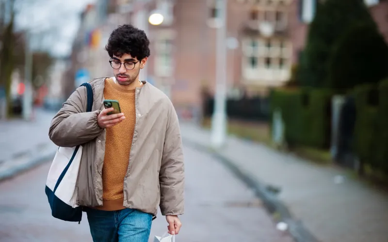 Een jonge man loopt op straat en kijkt naar zijn telefoon