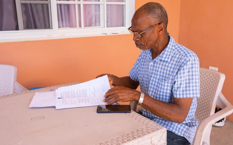 Man op Bonaire zit buiten aan een tafel en lees brieven van de overheid