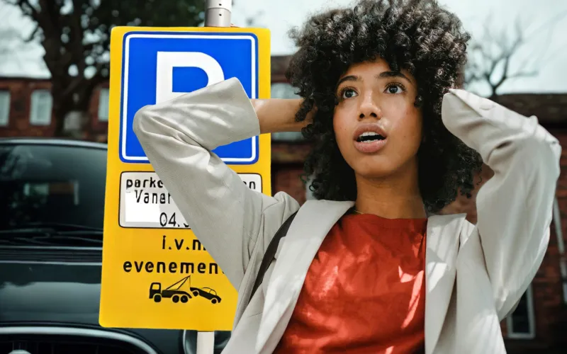 Jonge vrouw staat voor bord parkeerverbod en kijkt verbaasd met haar handen in het haar.