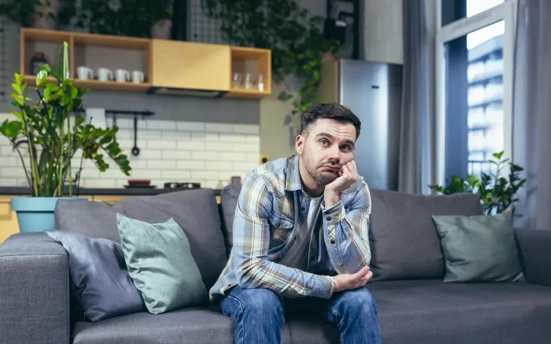 Man zit op de bank en baalt van een foutieve WOZ berekening van zijn huis 