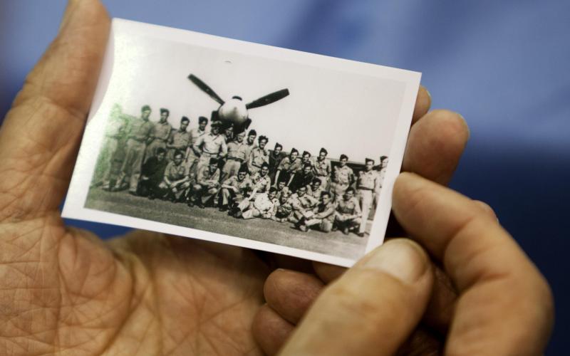 persoon houdt oude foto vast met militairen voor een vliegtuig
