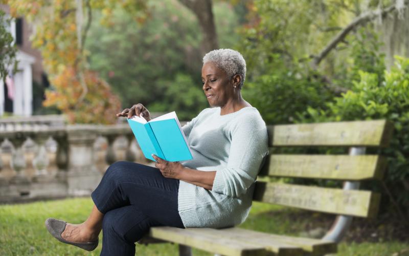 dame leest een boek, zittend op een bankje in het park