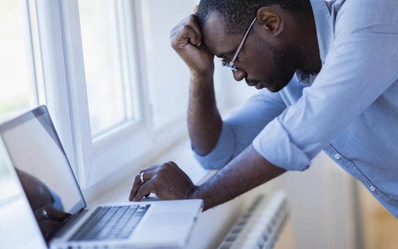 man met bril heeft hand onder zijn hoofd en kijkt op laptop