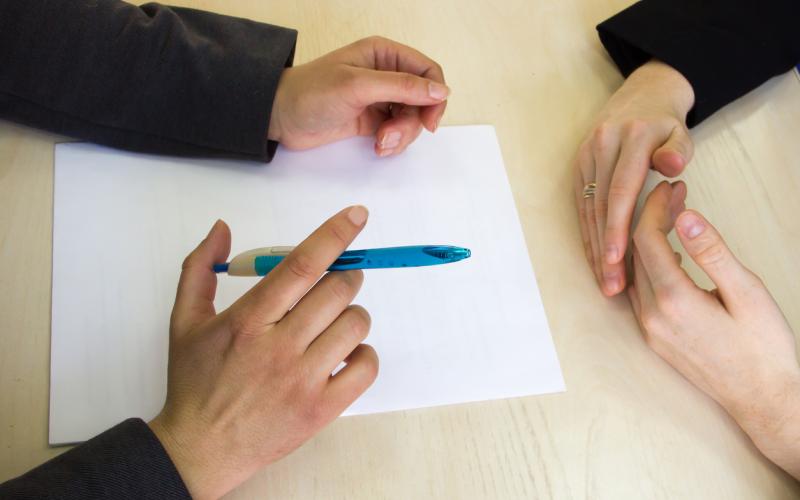Close up van twee mensen die tegenover elkaar aan tafel zitten, je ziet alleen hun handen