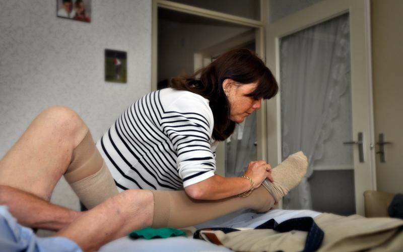 Een vrouw van thuishulp doet steunkousen aan bij een bejaarde man Een vrouw van thuishulp doet steunkousen aan bij een bejaarde man