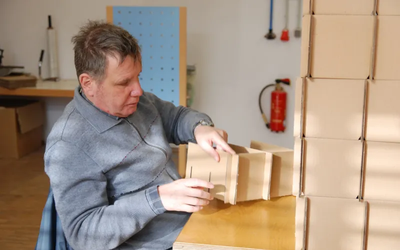 Foto van een man met beperking die een kartonnen doos in elkaar zet