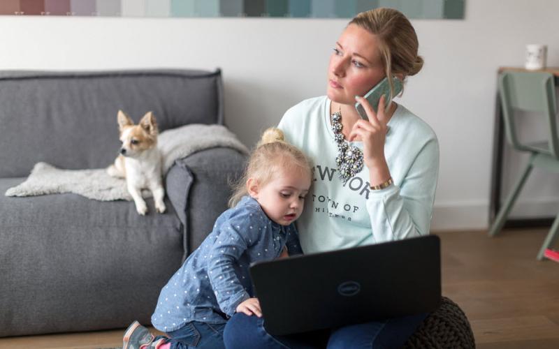 Een vrouw aan de telefoon met een laptop en een kind op schoot