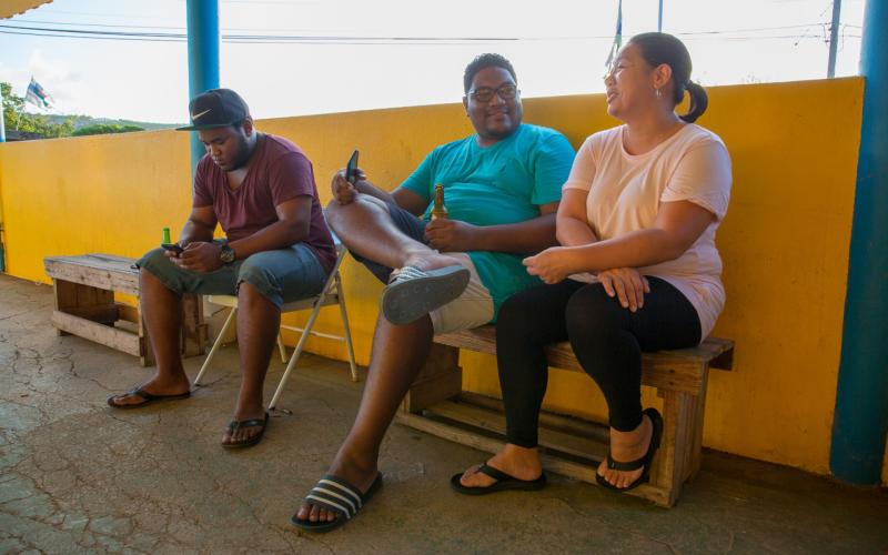 Drie personen zitten op een bankje en kletsen met elkaar. De foto is genomen op Bonaire.