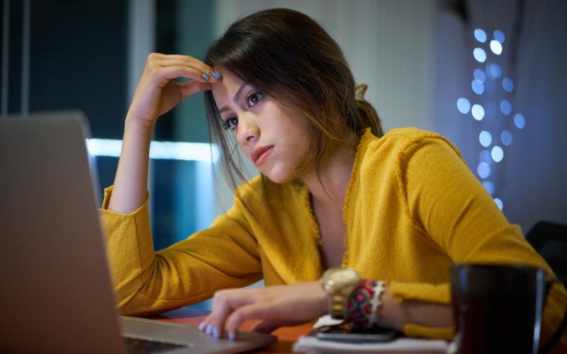 Jonge vrouw kijkt zorgelijk voor zich uit achter haar bureau