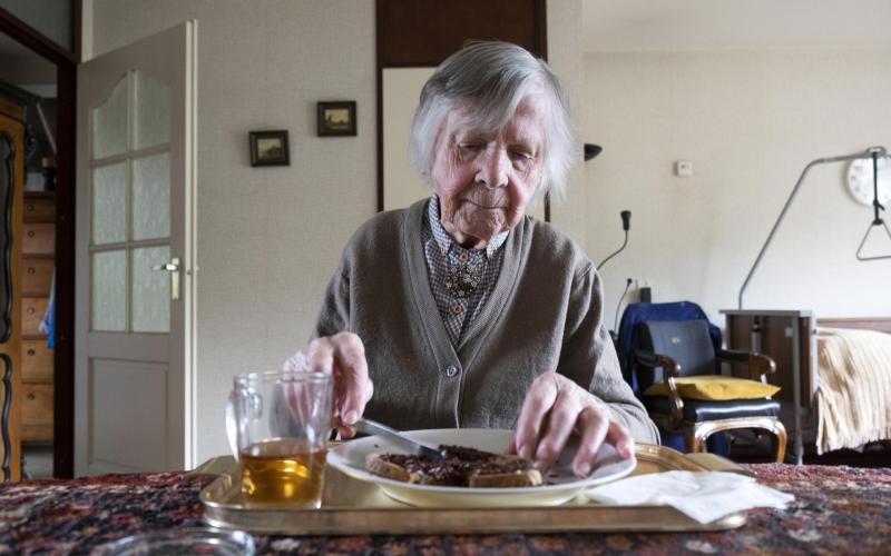 Oudere vrouw smeert een boterham thuis aan tafel