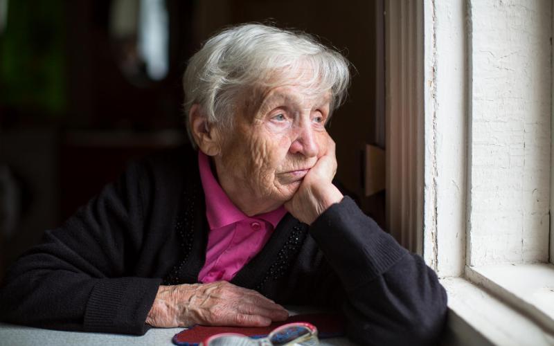 Een oude vrouw kijkt uit het raam terwijl haar kin op haar hand steunt