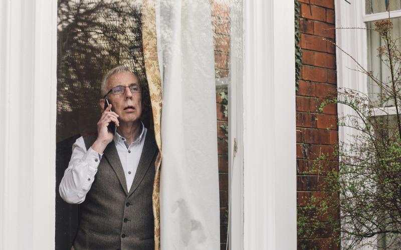 Een oudere man bij het raam met telefoon Een oudere man bij het raam met telefoon