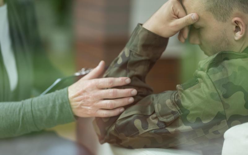 Een veteraan leunt met hoofd op hand en iemand troost hem