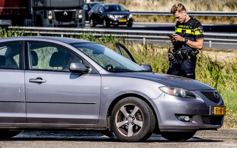 Een agent staat naast een auto bij een drukke weg en schrijft een boete uit. 