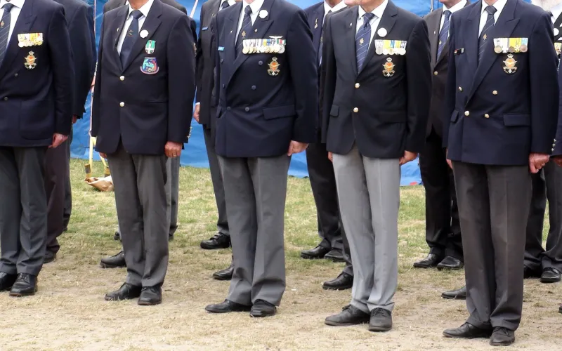 Een aantal veteranen op een rij. Ze zijn zichtbaar vanaf hun hals tot hun voeten. Ze dragen allemaal een pak.