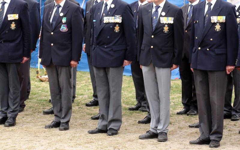 Een aantal veteranen op een rij. Ze zijn zichtbaar vanaf hun hals tot hun voeten. Ze dragen allemaal een pak.