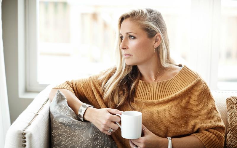 Vrouw kijkt voor zich uit met kop koffie in haar handen