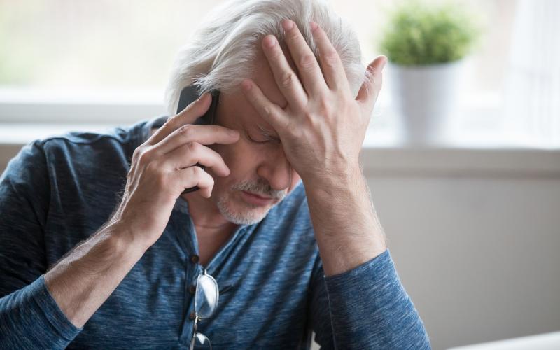 man zit wanhopig aan de telefoon met hand voor ogen