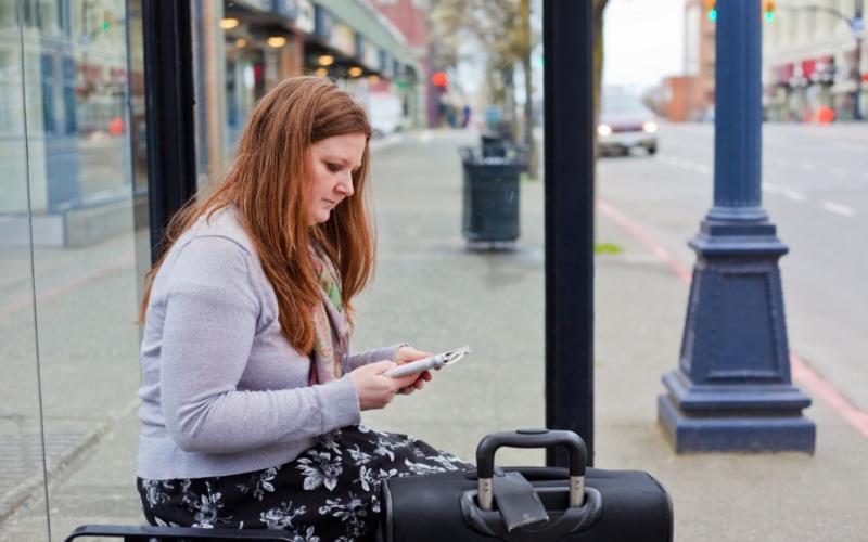 Vrouw zit met koffer bij bushalte