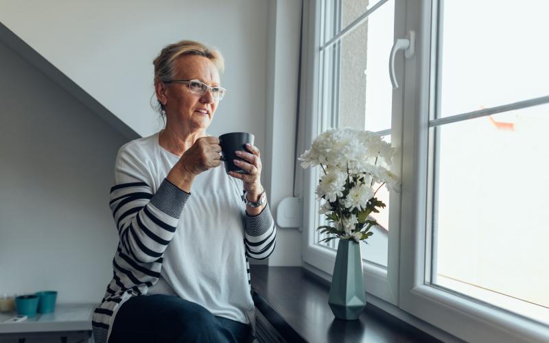 Vrouw zit bij het raam met een kop koffie