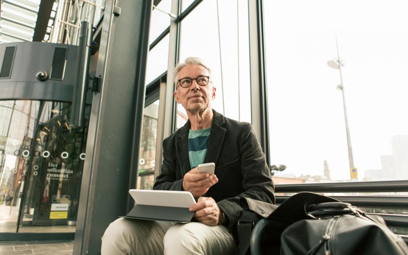 Man zit op bankje met koffer en werktas Man zit op bankje met koffer en werktas