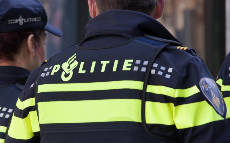 Een politie agent van de achterkant gefotografeerd. We zien zijn rug en politiekleding.