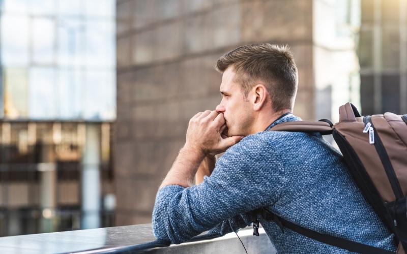 Jongeman met rugzak op rug houdt handen onder kin Jongeman met rugzak op rug houdt handen onder kin