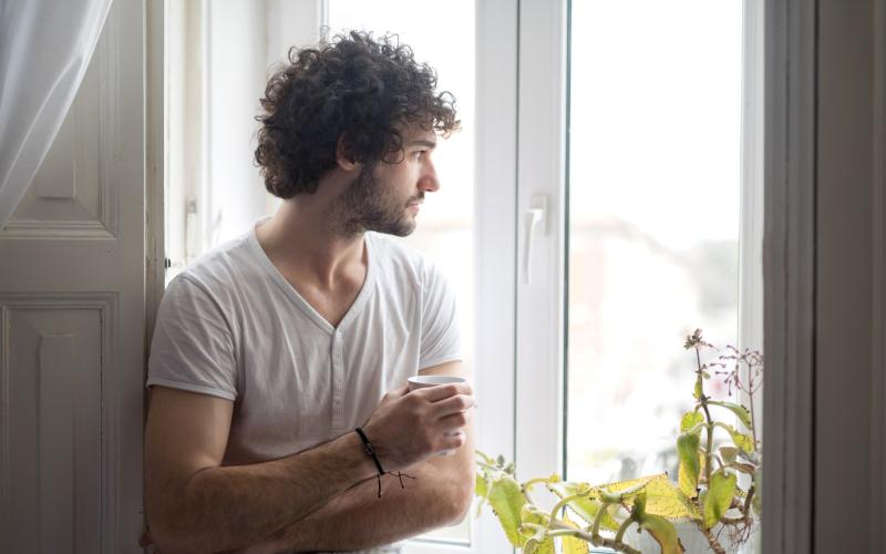 Man met kop koffie kijkt uit het raam