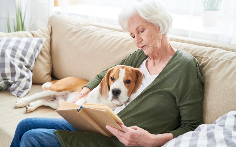 Vrouw zit met hond op de bank een boek te lezen