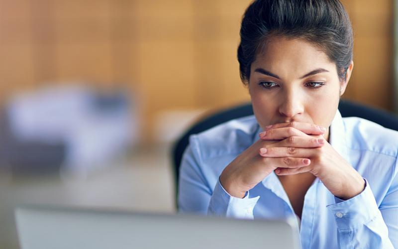 Vrouw zit met gevouwen handen voor laptop Vrouw zit met gevouwen handen voor laptop