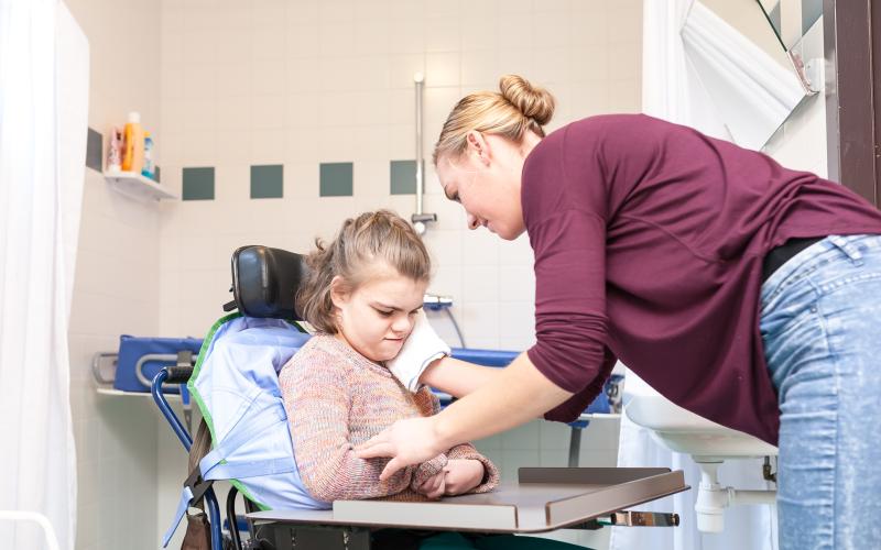 Verzorgster helpt meisje in rolstoel met wassen van het gezicht Verzorgster helpt meisje in rolstoel met wassen van het gezicht