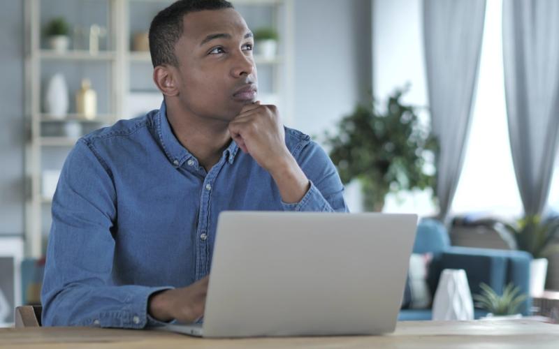 Man zit achter zijn laptop en kijkt bedenkend omhoog Man zit achter zijn laptop en kijkt bedenkend omhoog