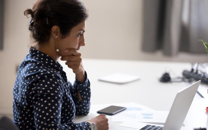 Mevrouw met papieren en telefoon voor zich achter de laptop