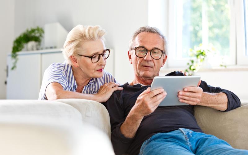 Ouder stel zit op de bank met iPad in de hand Ouder stel zit op de bank met iPad in de hand