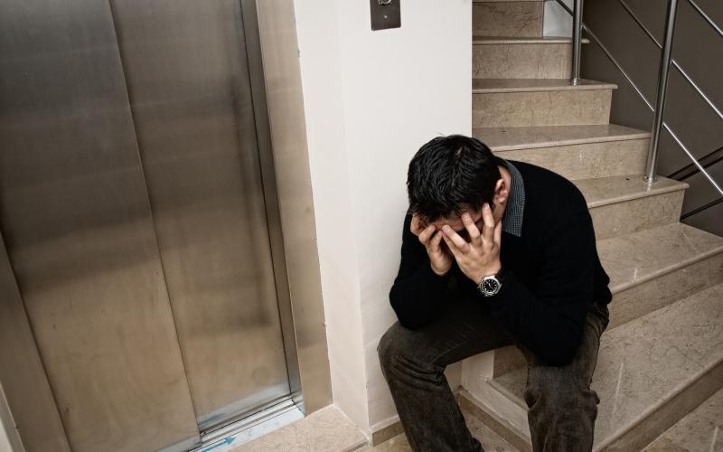Man zit in trappenhuis met handen voor gezicht en in het haar Man zit in trappenhuis met handen voor gezicht en in het haar