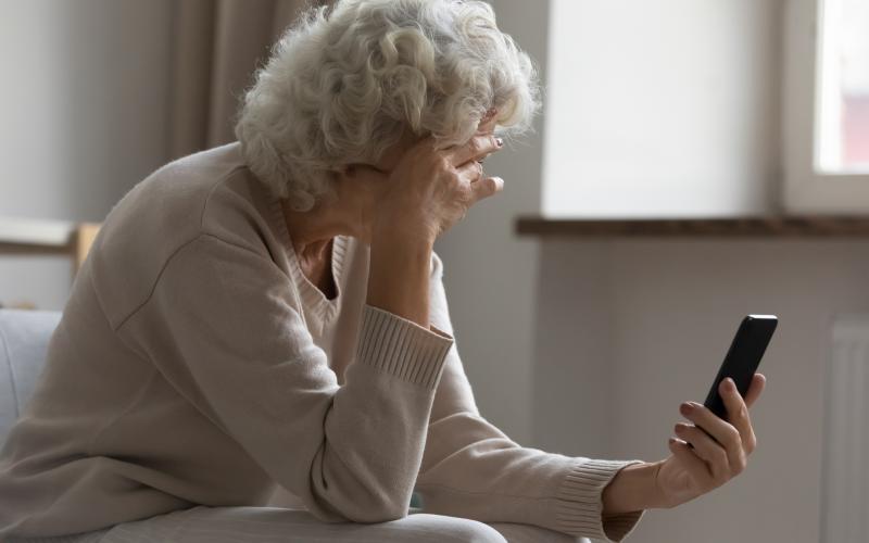 Een oudere vrouw met haar met smartphone in haar hand. Ze leunt met haar hoofd op haar andere hand. Een oudere vrouw met haar met smartphone in haar hand. Ze leunt met haar hoofd op haar andere hand.