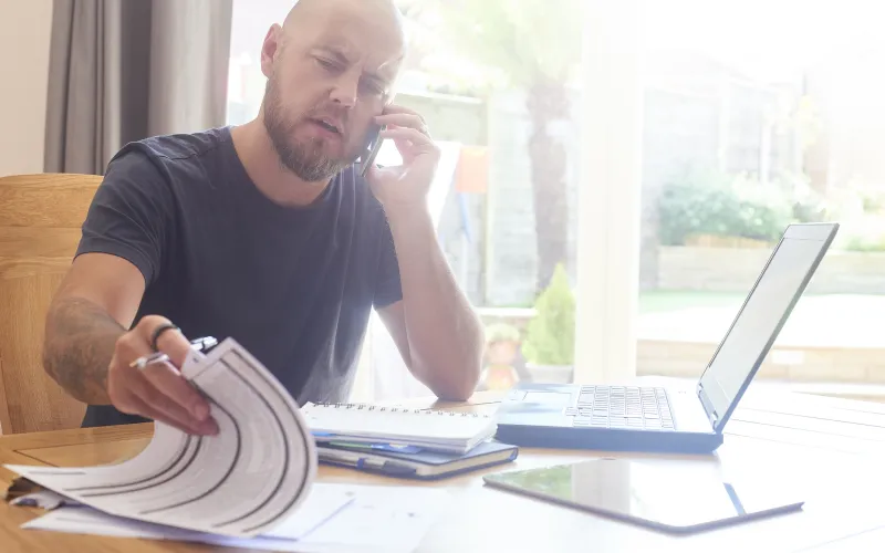 Bellende man aan tafel met laptop en papieren voor zich