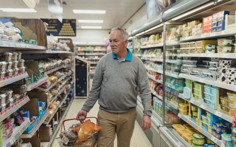 Senior man loopt met gevuld winkelmandje in supermarkt