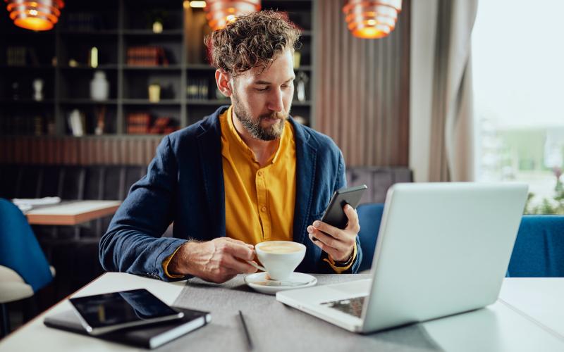 Man met kop koffie en telefoon in de hand in café