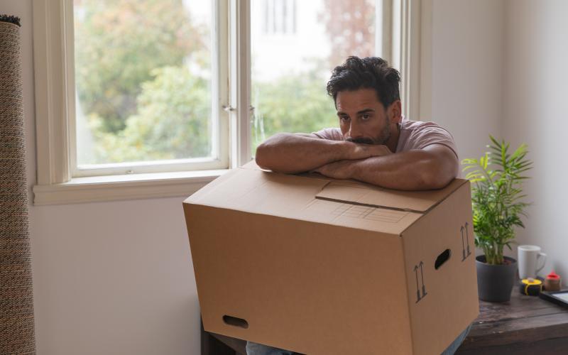 man kijkt vertwijfeld voor zich uit met verhuisdoos op schoot