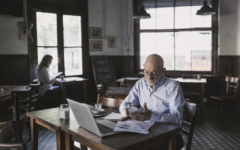 Zzp'er met laptop en papieren voor zich aan het werk in een café