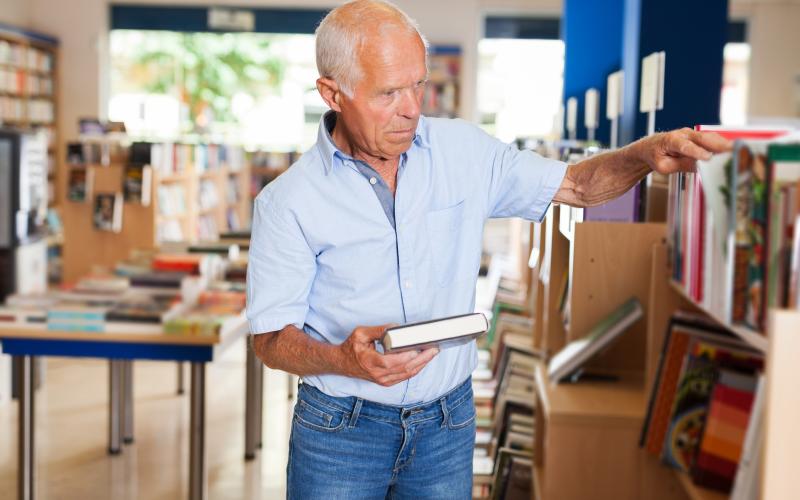 Senior man met boek in zijn hand in een boekenwinkel