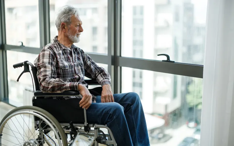 Man zit in rolstoel en kijkt uit het raam