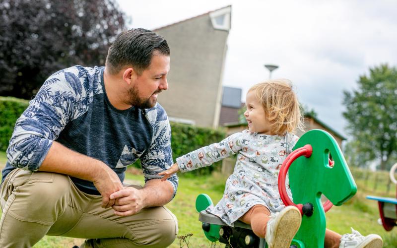 Jonge ouder man met zijn dochtertje in de speeltuin. Dochtertje zit op wipwap. Jonge ouder man met zijn dochtertje in de speeltuin. Dochtertje zit op wipwap.