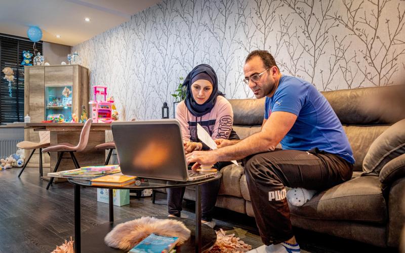 Man en vrouw zitten thuis op de bank. Voor zich hebben zij een laptop en in de hand papieren. Man en vrouw zitten thuis op de bank. Voor zich hebben zij een laptop en in de hand papieren.