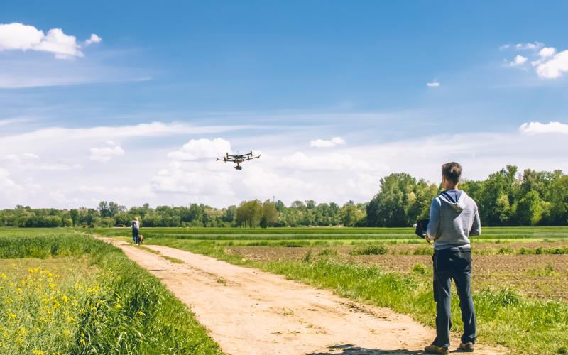 Man staat tussen twee grasvelden in en vliegt met zijn drone