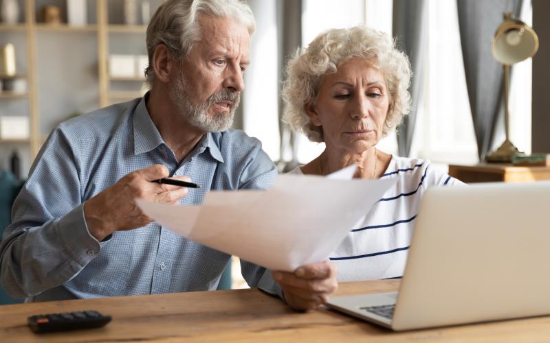 Ouder echtpaar zit achter een laptop en doet belastingaangifte
