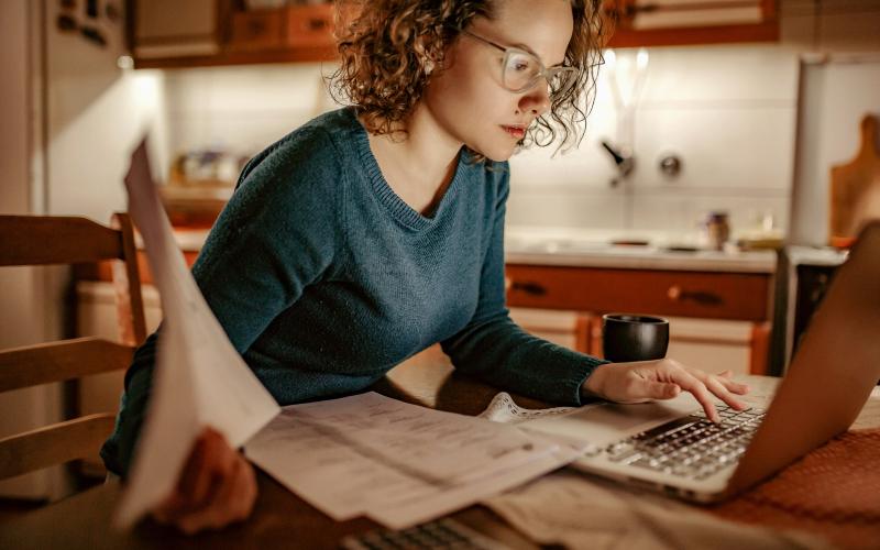 Jonge vrouw achter de computer met rekeningen in haar hand Jonge vrouw achter de computer met rekeningen in haar hand